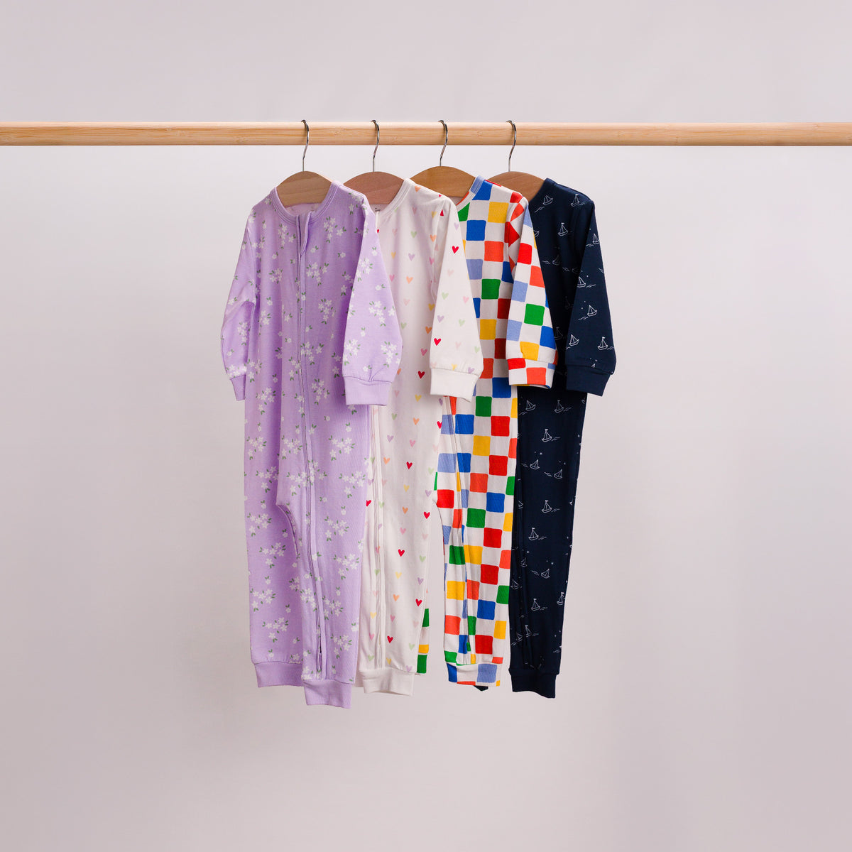 Hanging shot of 4 PJ Zipsuits. Lilac Daisy, Mini Hearts, Check and Sailboat.