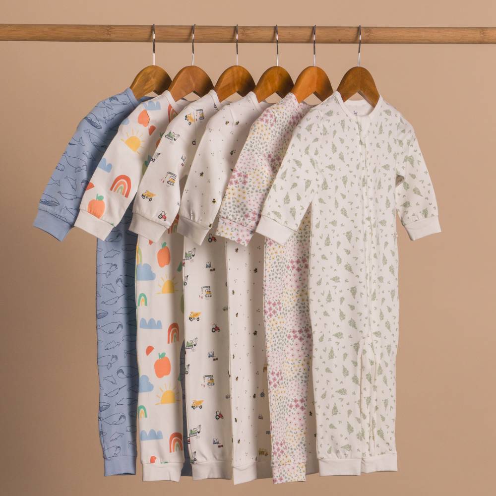 Set of baby onesies with various patterns hanging on a rack against a beige background