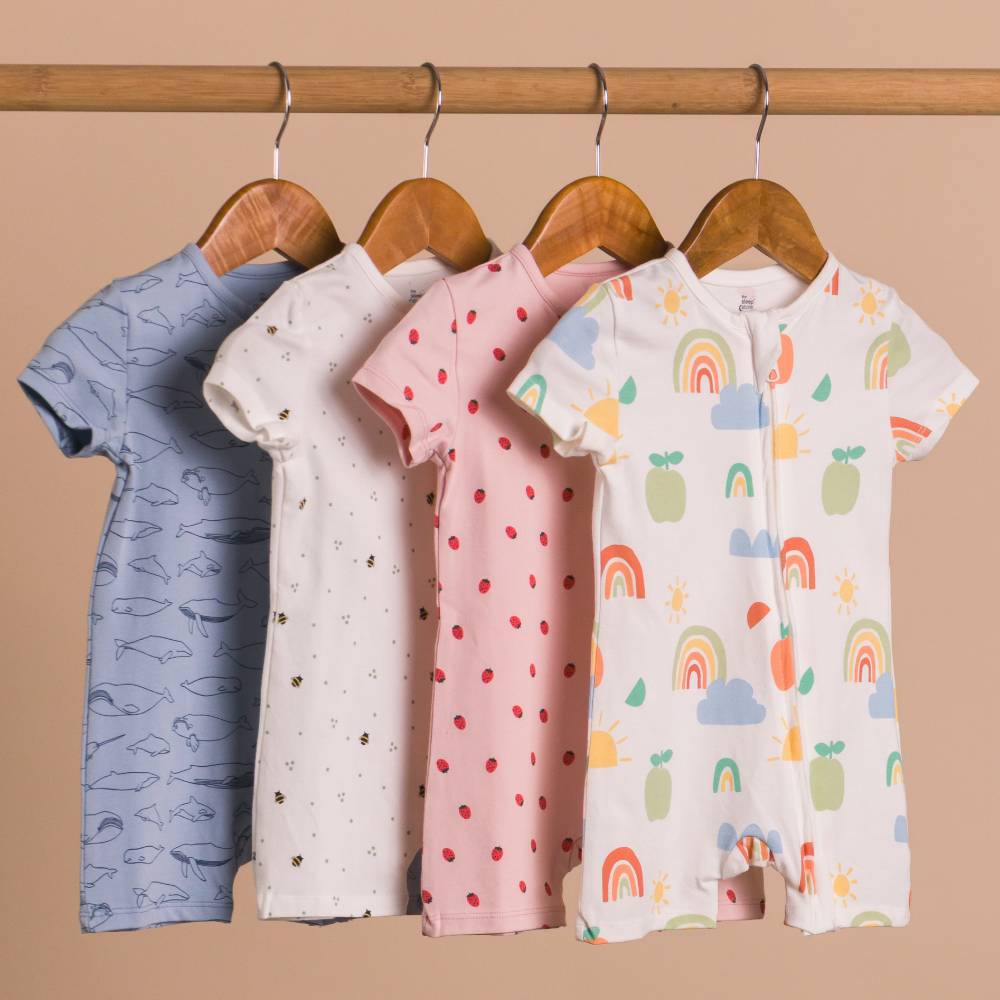 Four children's onesies with different patterns hanging on a wooden rod against a beige background.
