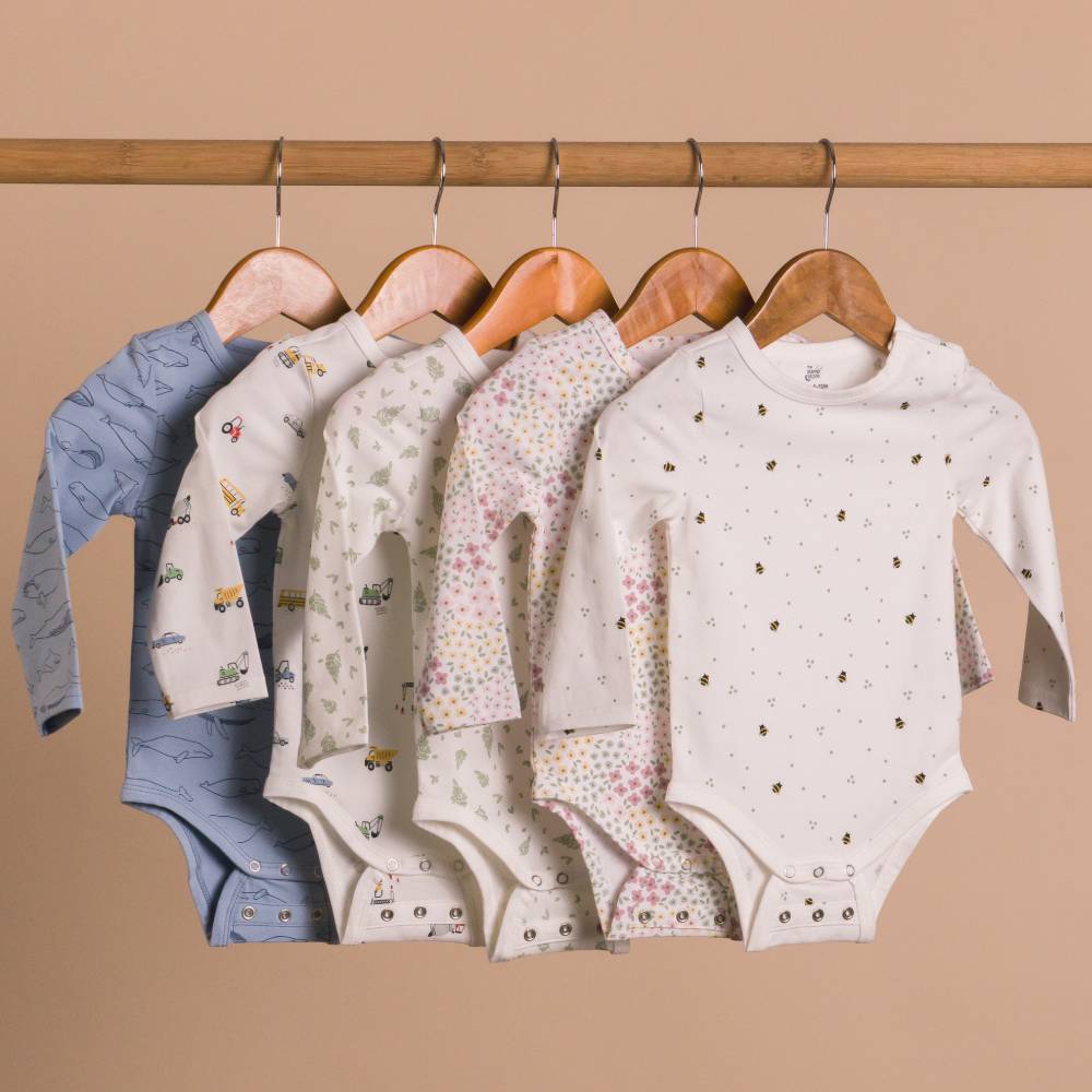 Collection of baby cotton onesies on hangers against a beige background