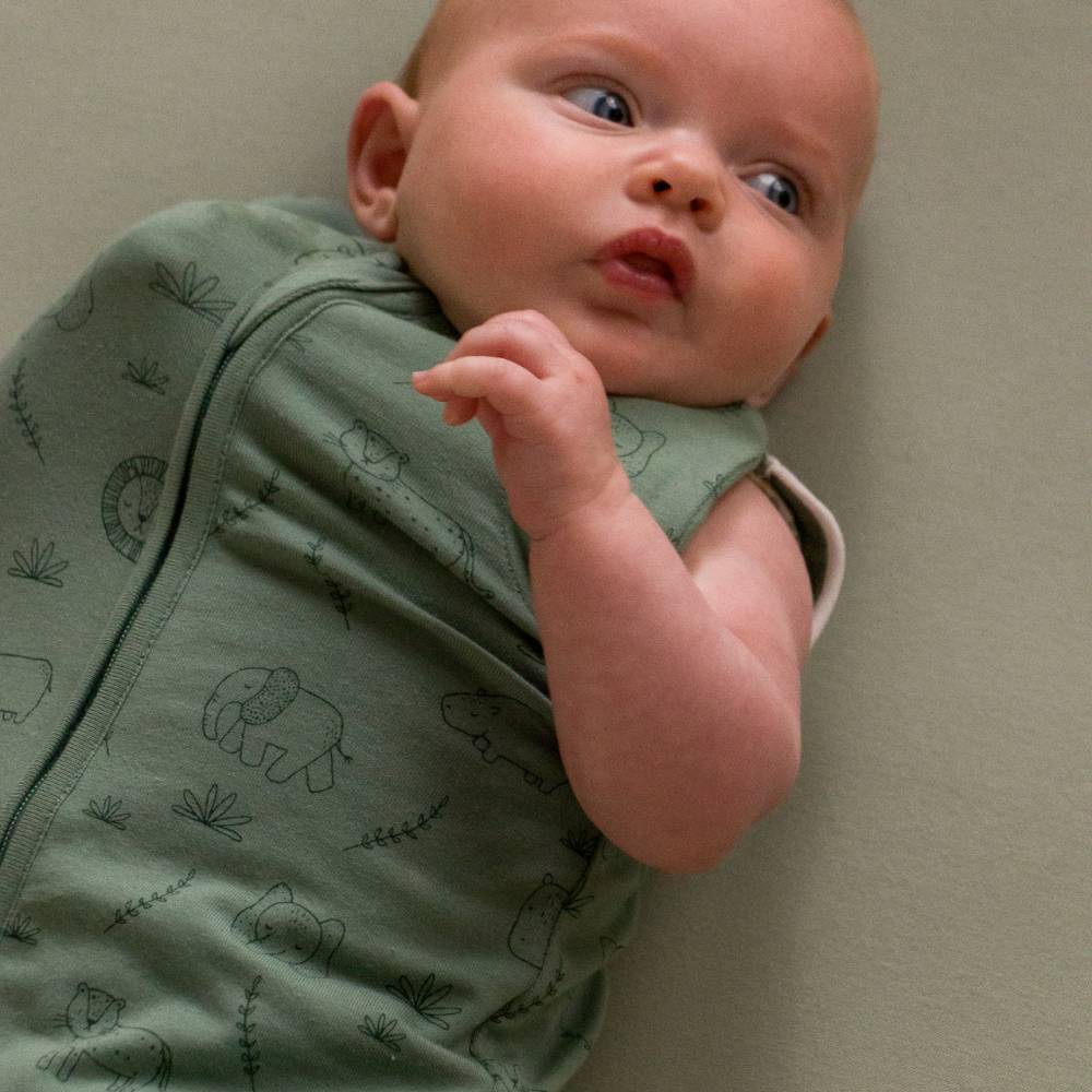 Baby wearing a green outfit with animal patterns on a beige background