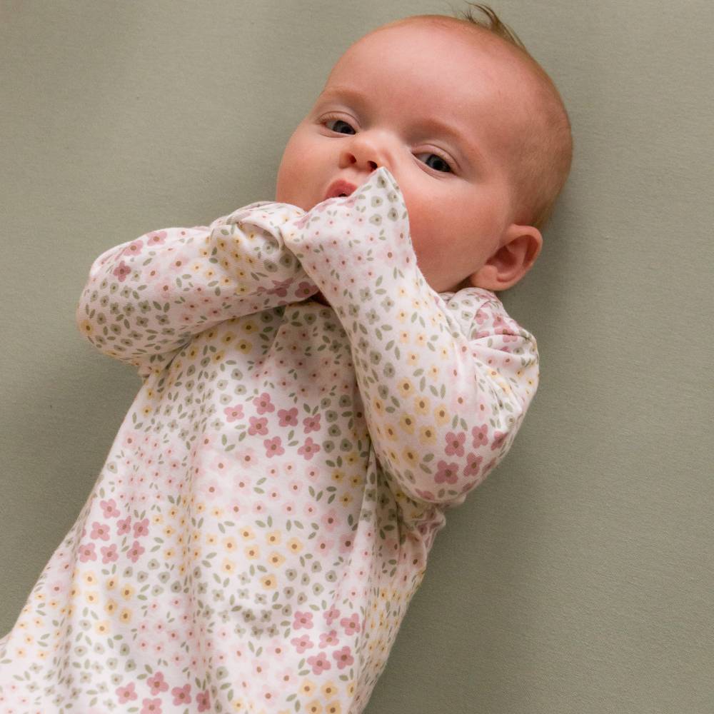 Baby in a cotton floral knotted gown against a plain background