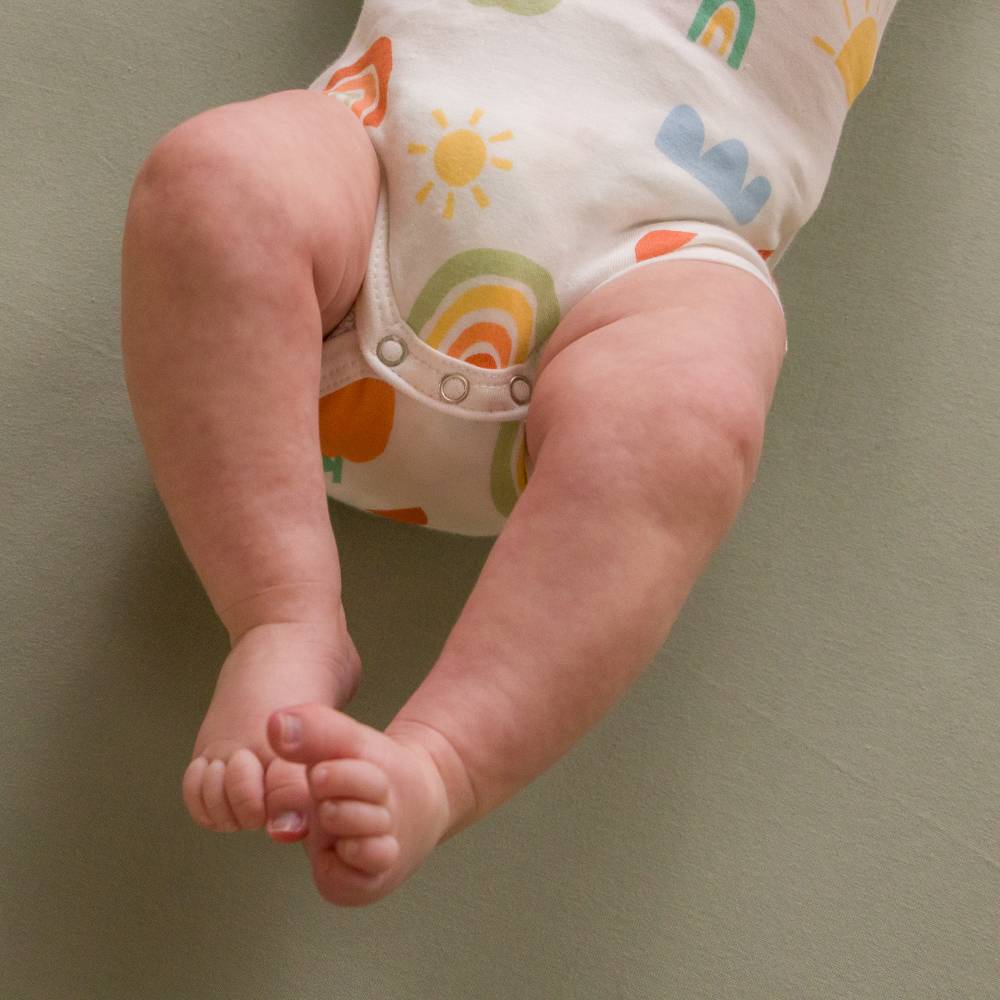 Baby legs and feet wearing a colorful diaper against a plain background