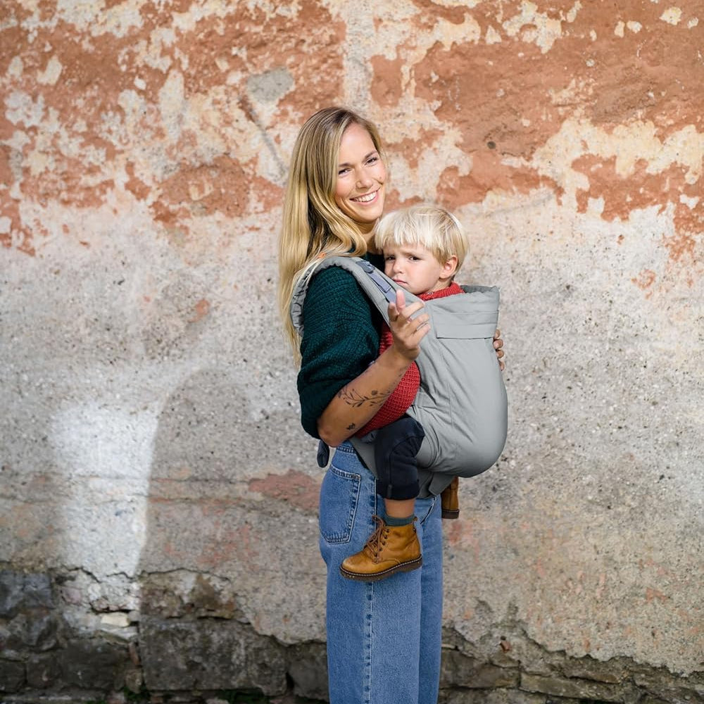 Woman holding a child against a textured wall in a beco Toddler Carrier