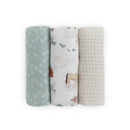 Three rolled muslin swaddle blankets standing upright on a white background. The left blanket is sage green with white leaf patterns.