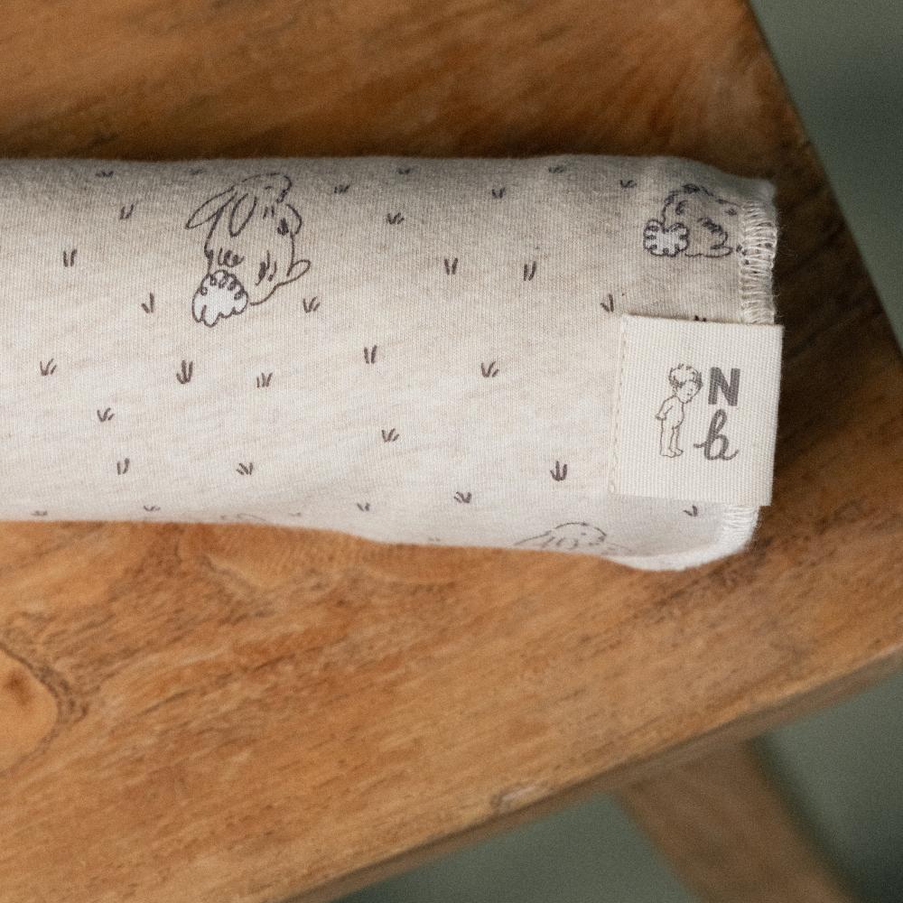Rolled-up beige cotton jersey fabric with animal prints on a wooden surface, featuring a Nature Baby brand label.