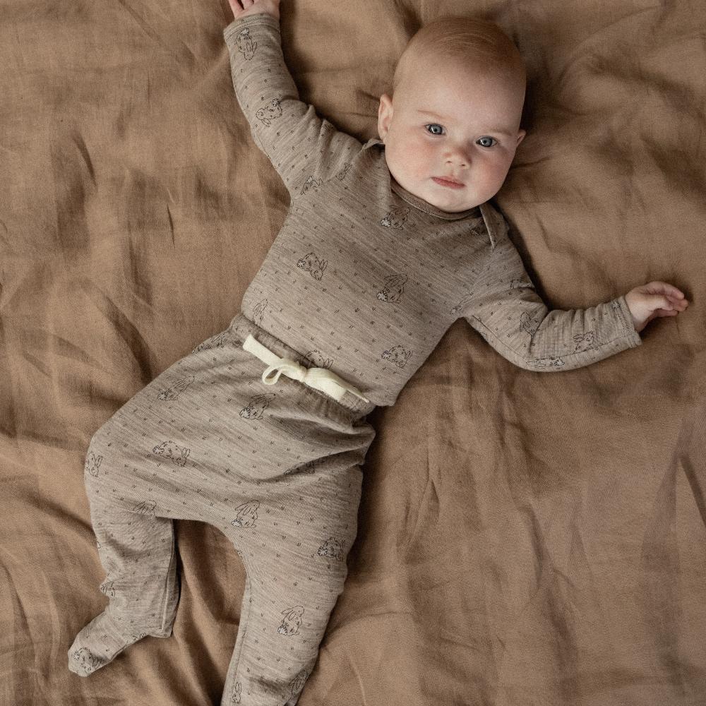 Baby in a brown merino bunny design matching outfit lying on a brown blanket