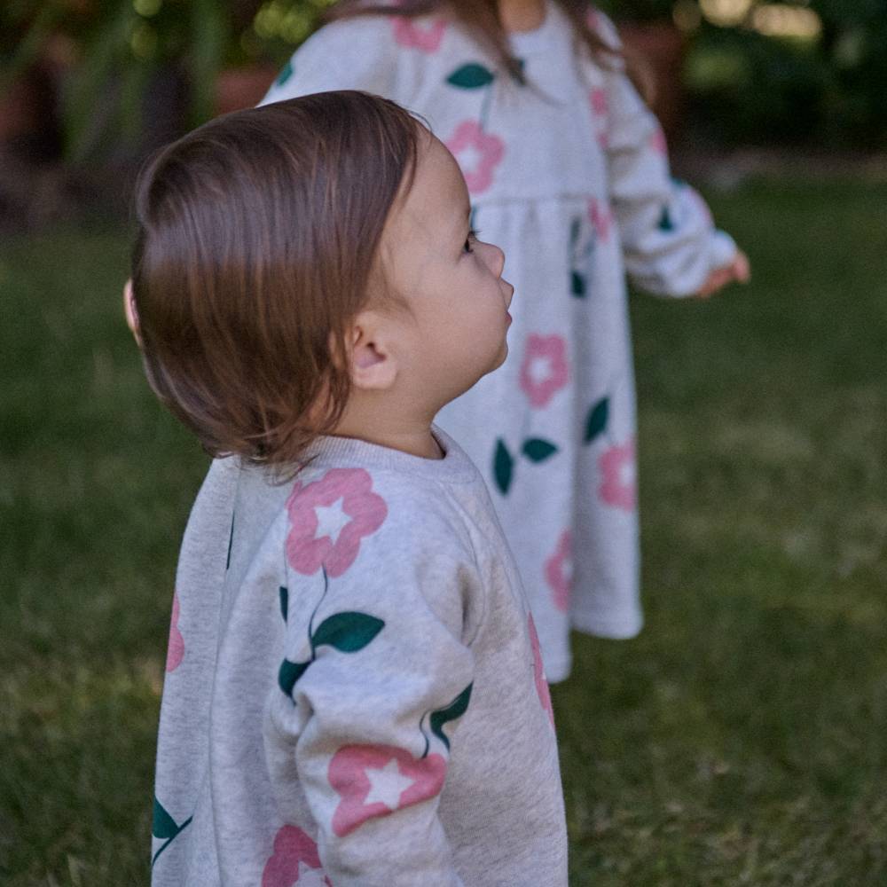 Two children wearing beige marl floral outfits standing on grass