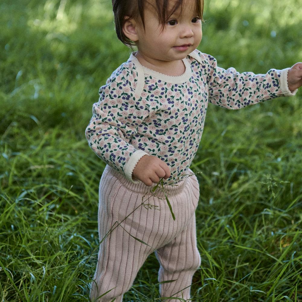 Child in a Nature Baby cotton floral bodysuit and light pink pants standing in grass