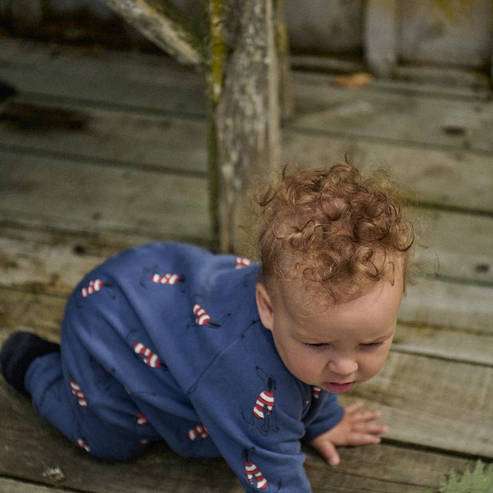 Child in a blue outfit with red and white dog patterns on a wooden deck