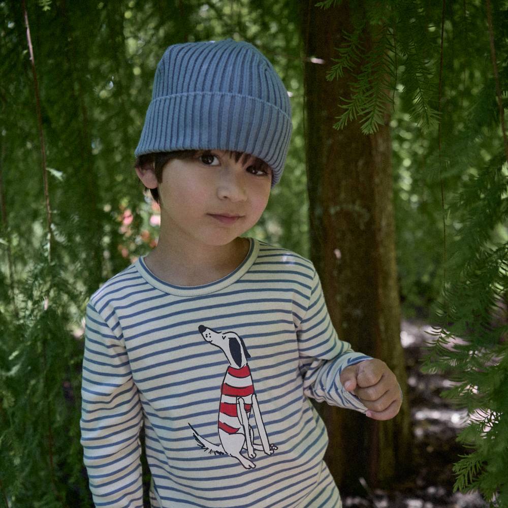 Child wearing a blue knit hat and striped shirt with a dog graphic in a forest setting