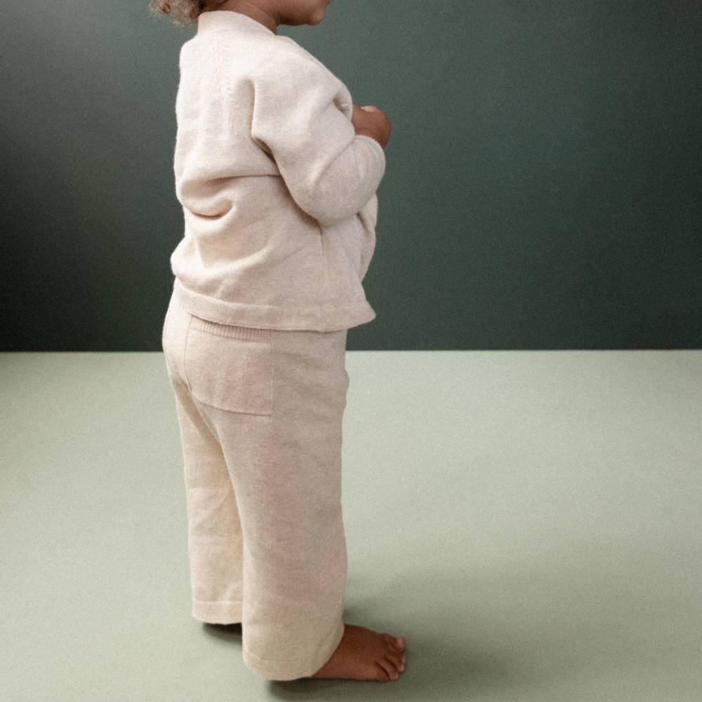Child wearing a cosy beige knitted outfit against a plain background