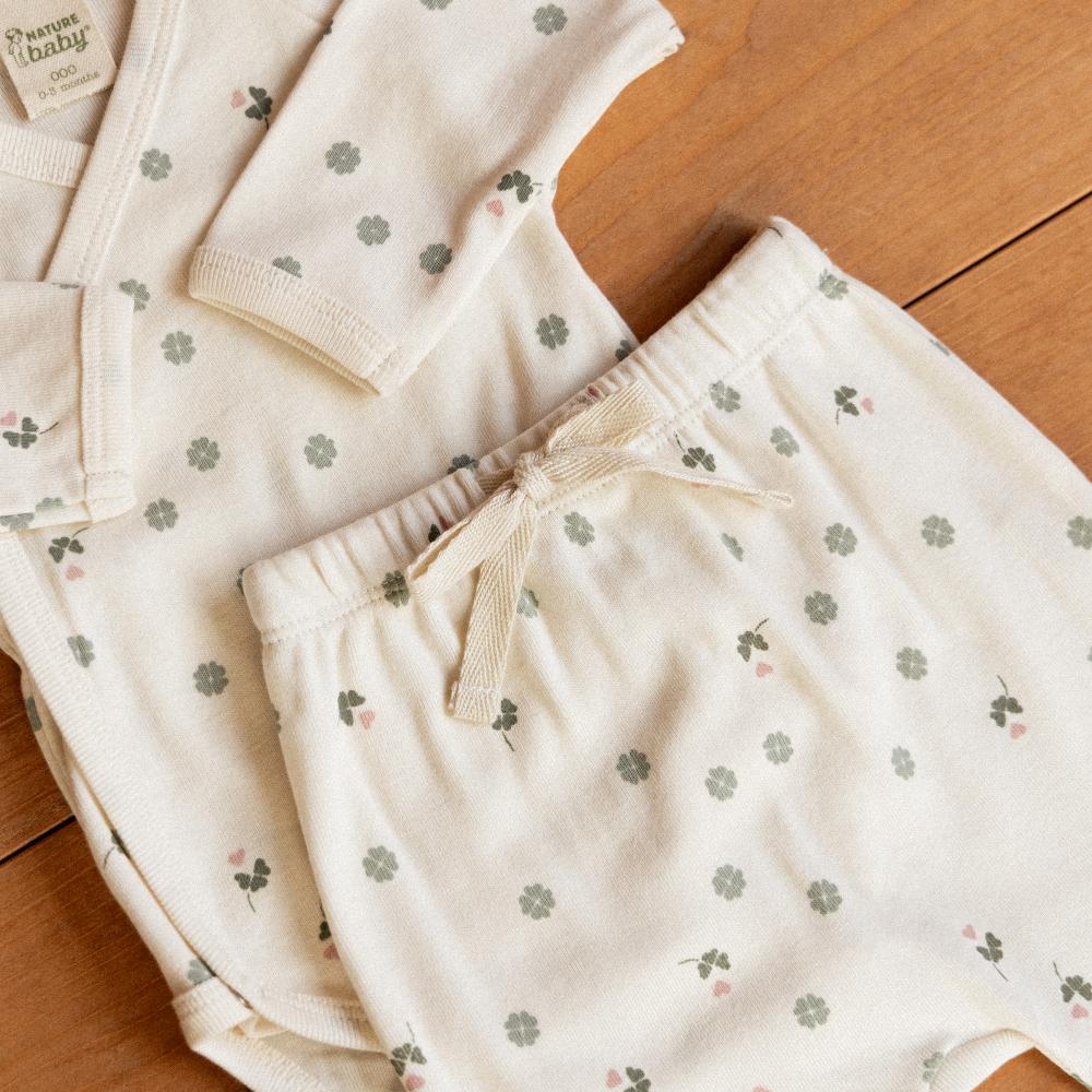 Long-sleeve bodysuit and matching footed romper pants with clover pattern on a wooden floor