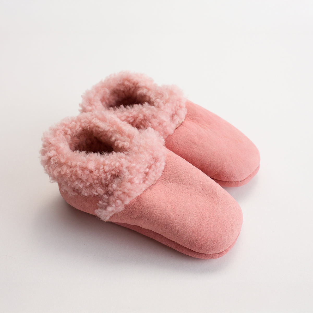 Pair of pink woolbabe lambskin slippers with fuzzy trim on a light background
