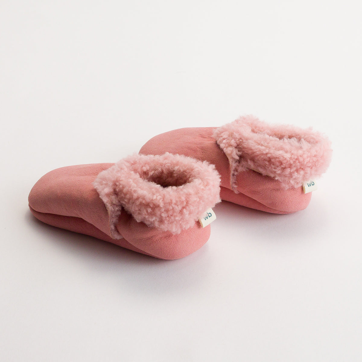 Pair of pink woolbabe children's slippers with fluffy wool lining and woolbabe tag on a white background