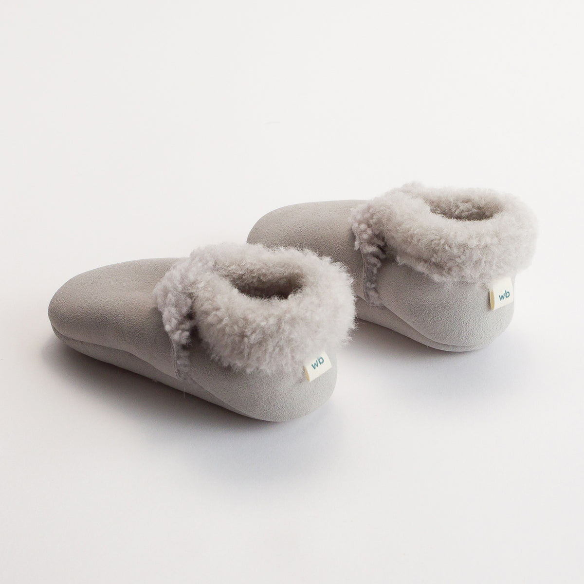 Pair of gray woolbabe children's wool slippers with fluffy trim on a white background