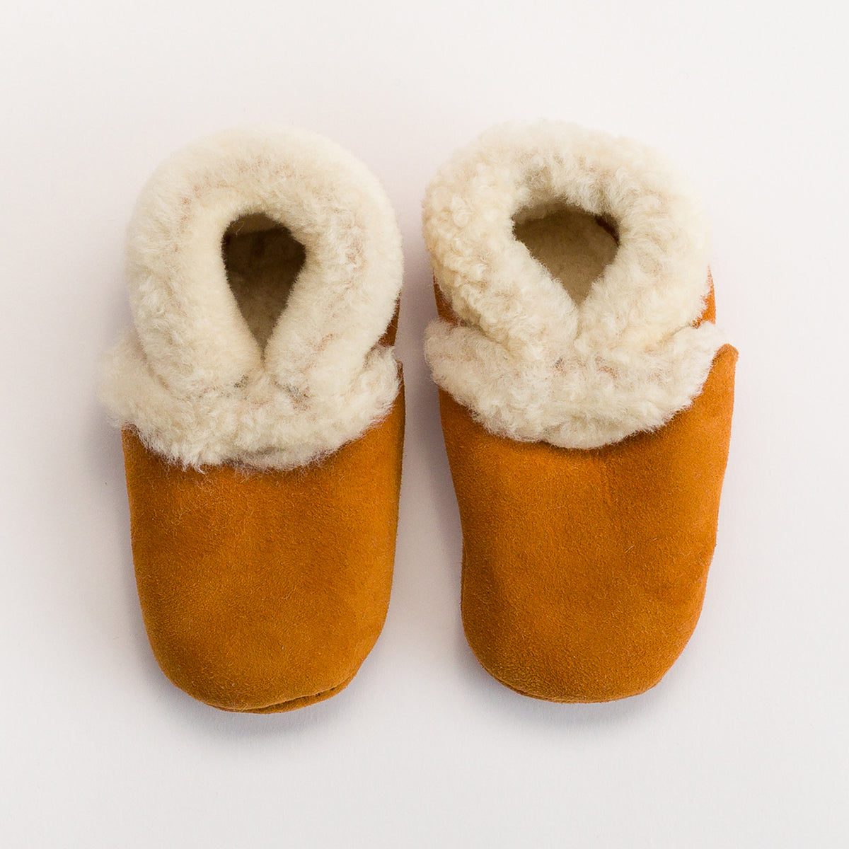 Pair of brown slippers with white fur lining on a light gray background