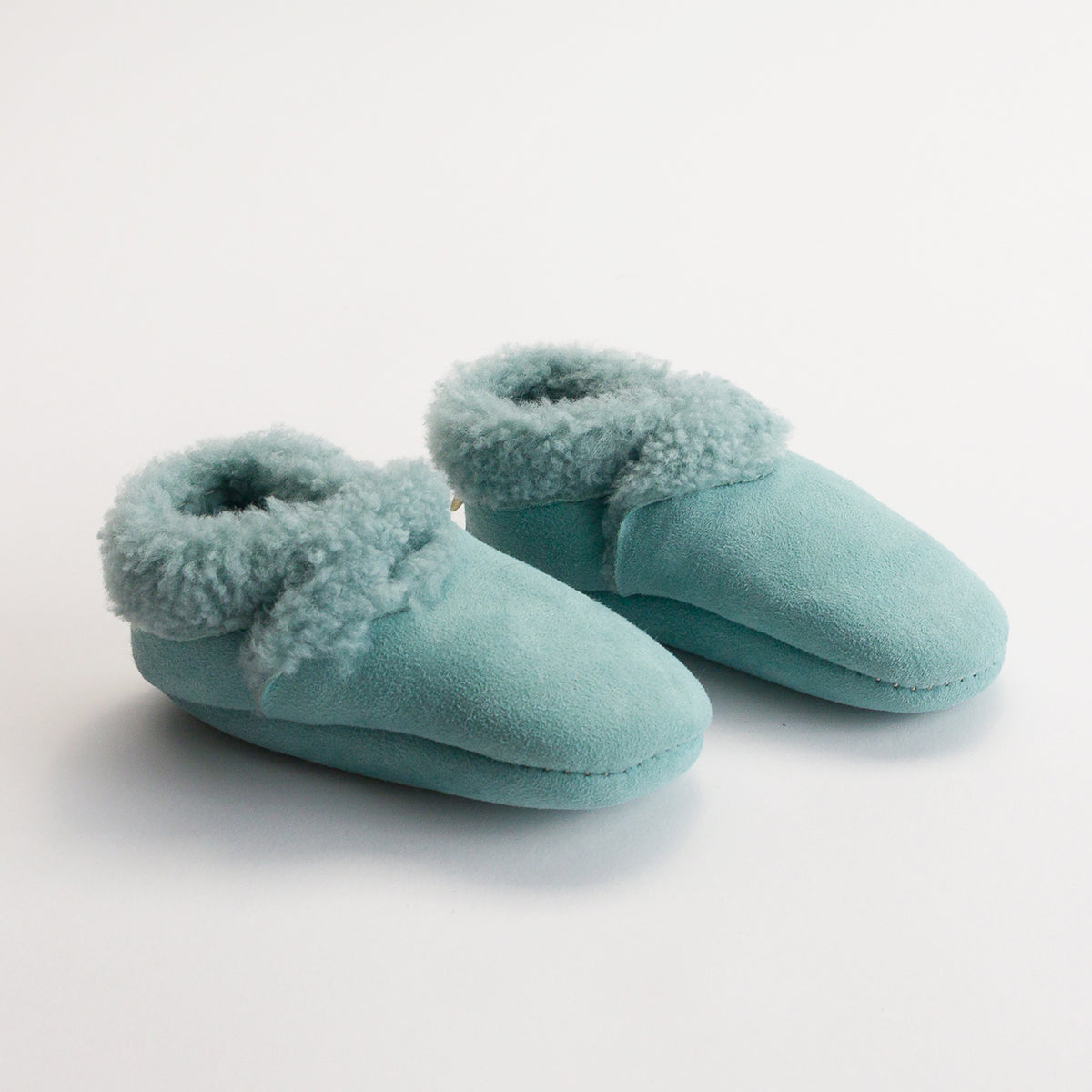 Pair of teal slippers with fuzzy wool trim on a white background