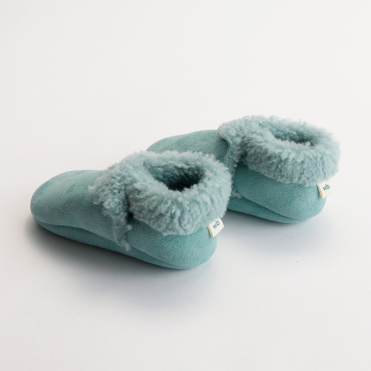 Pair of tide coloured woolbabe lambkins booties on a light gray background