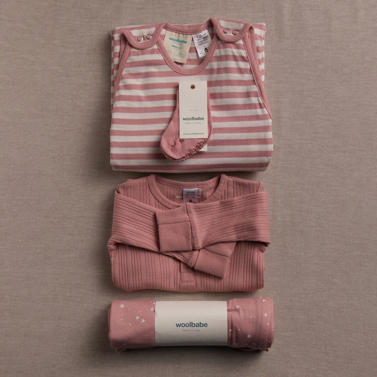 Folded baby clothing set with 'woolbabe' label on a beige background