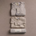 Folded woolbabe baby clothing items with tags on a beige background