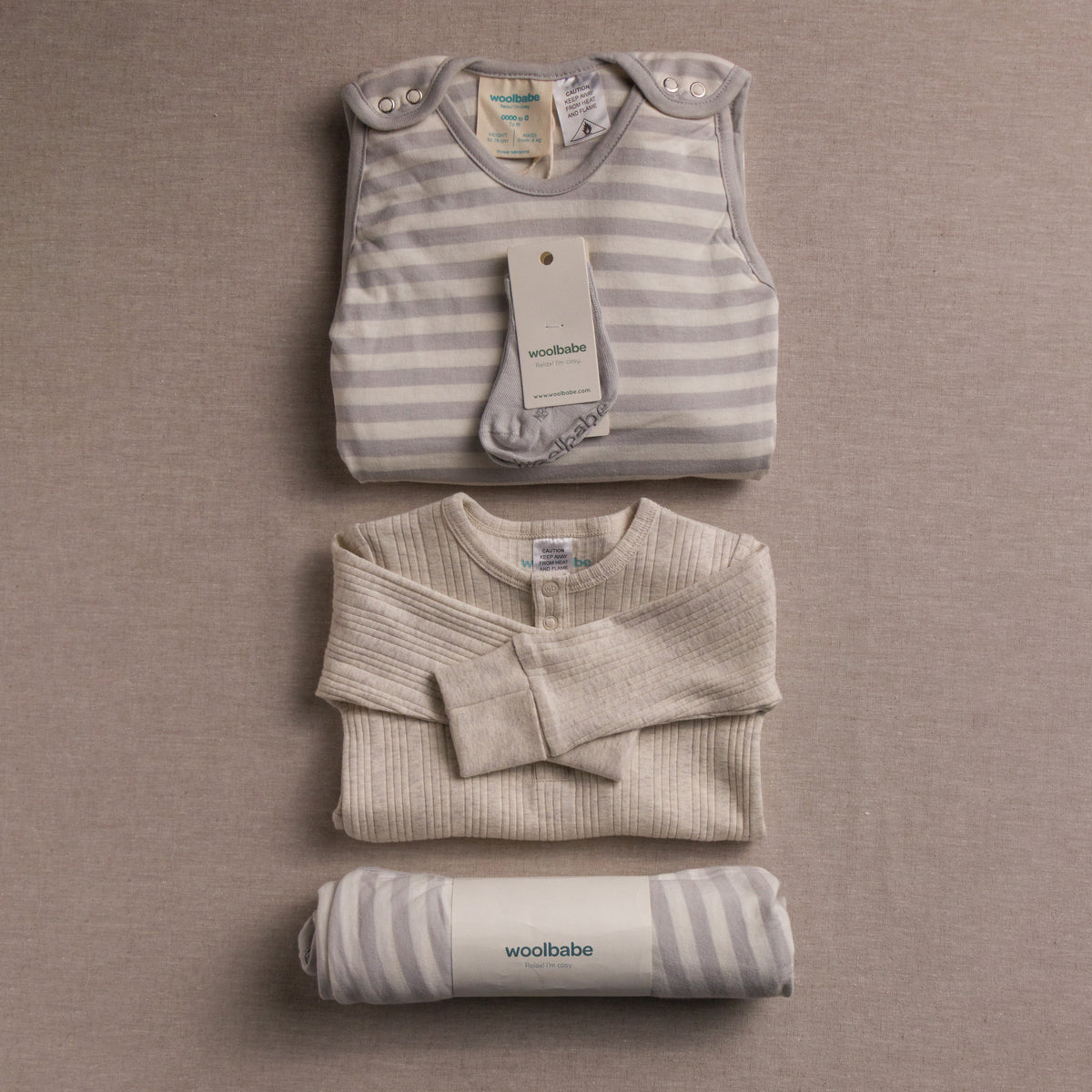 Folded woolbabe baby clothing items with tags on a beige background