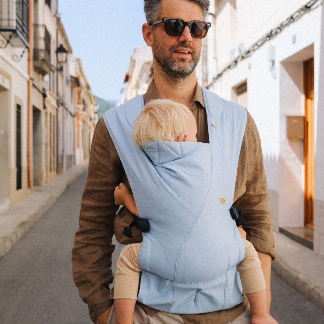 A front shot of a man wearing a light blue baby carrier with a child inside. 