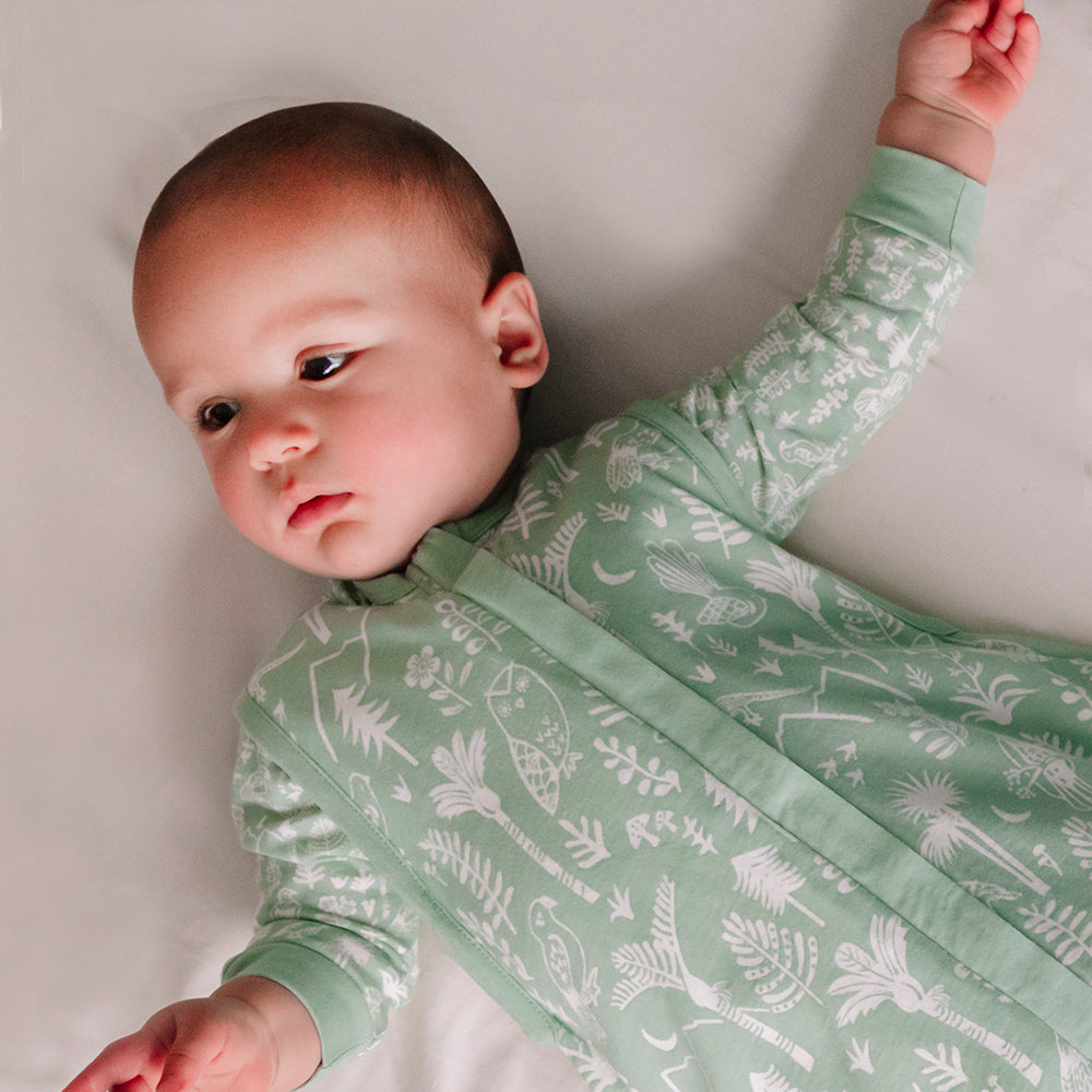 Baby wearing a green long-sleeve shirt with white patterns under a woolbabe sleep sack on a plain background