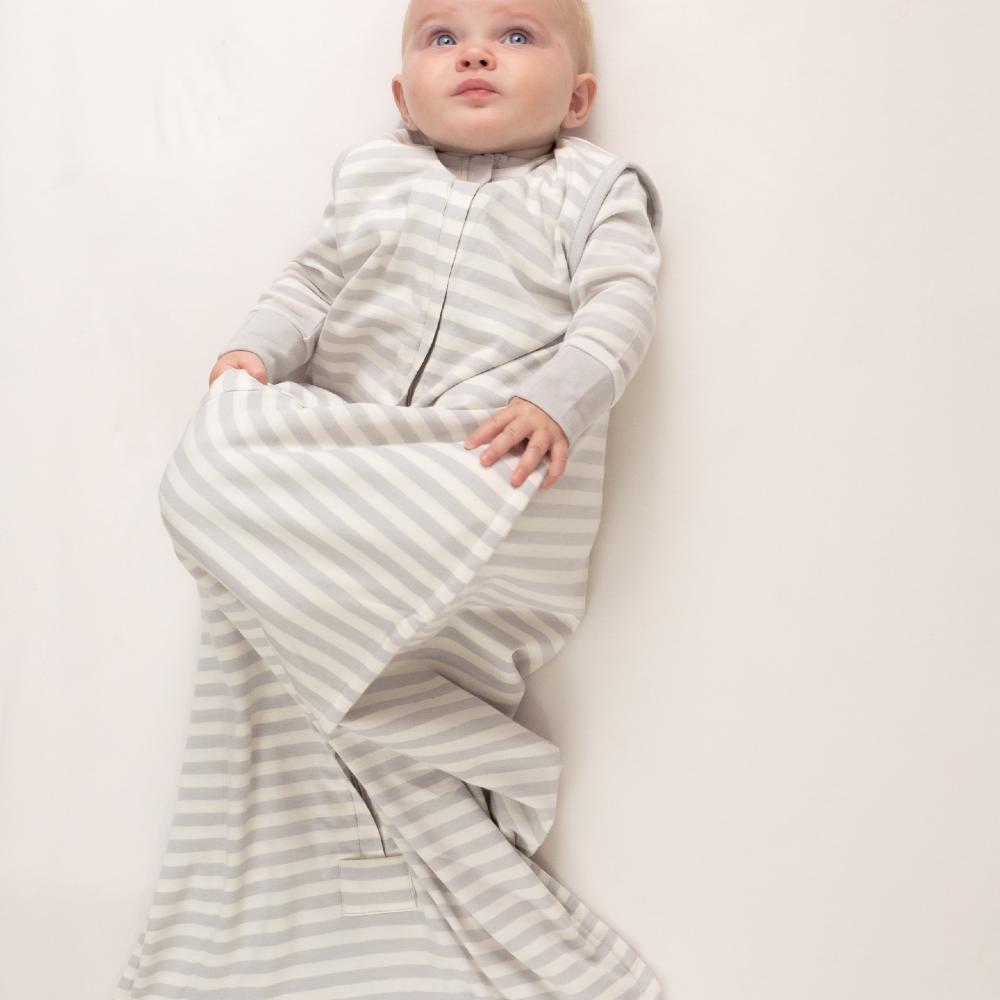 Baby wrapped in a gray and white striped sleeping bag on a light background