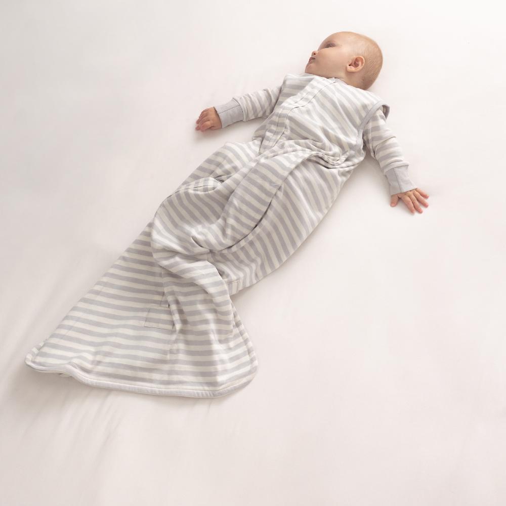 Baby lying on a white surface wearing a gray and white striped sleep sack from woolbabe.