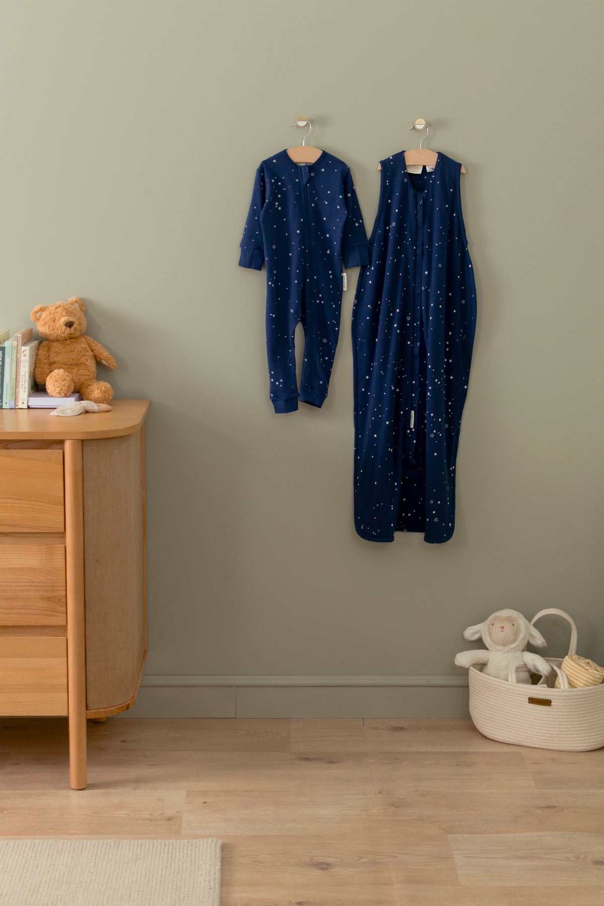 Navy blue children'swoolbabe sleeping bags with star pattern hanging on a wall next to a wooden dresser with toys.