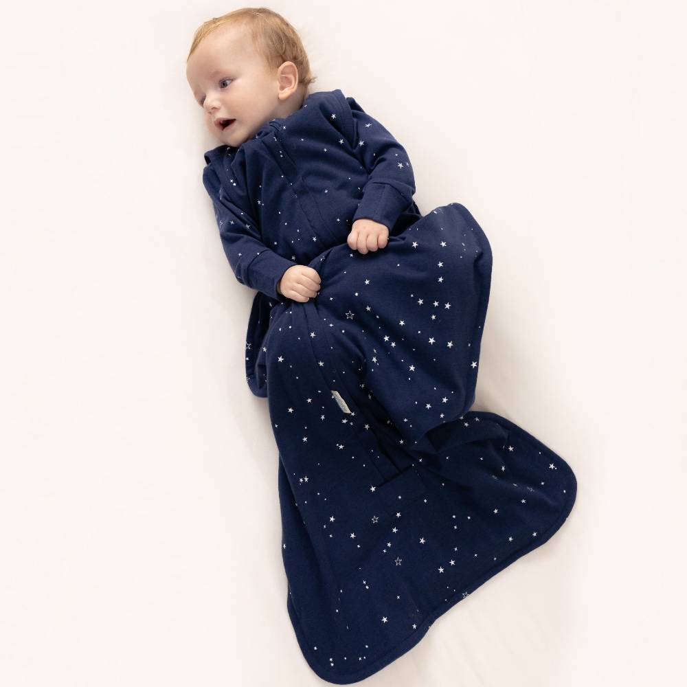 Baby wrapped in a navy blue baby sleeping sack with star pattern on a white background