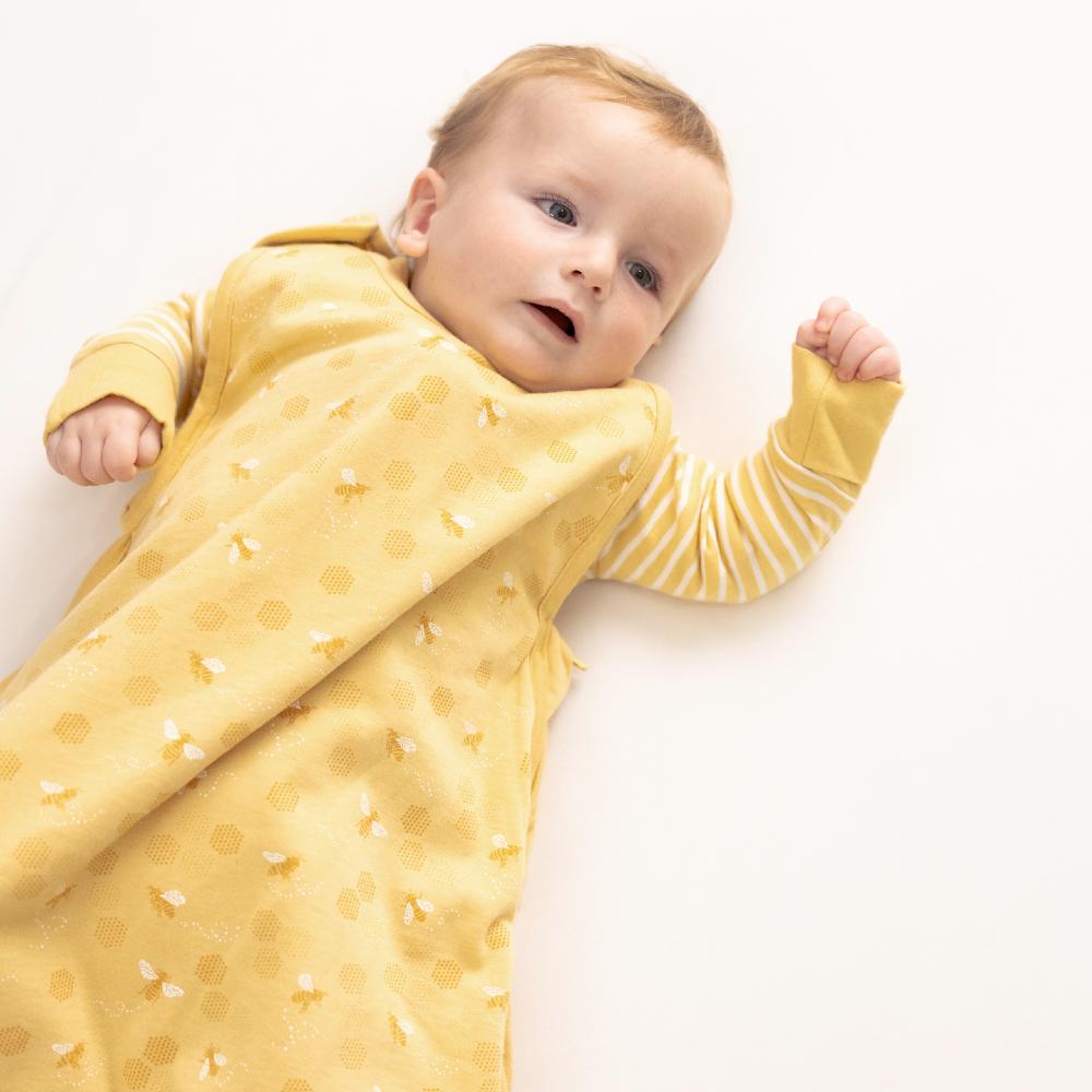 Baby wrapped in a yellow sleep sack with white patterns on a white background