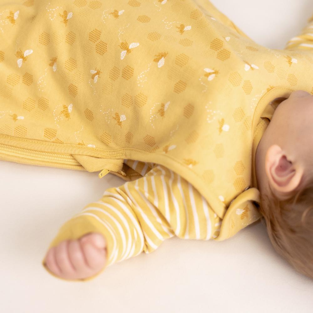 Baby lying on a white surface wearing a yellow bee print woolbabe sleep sack 