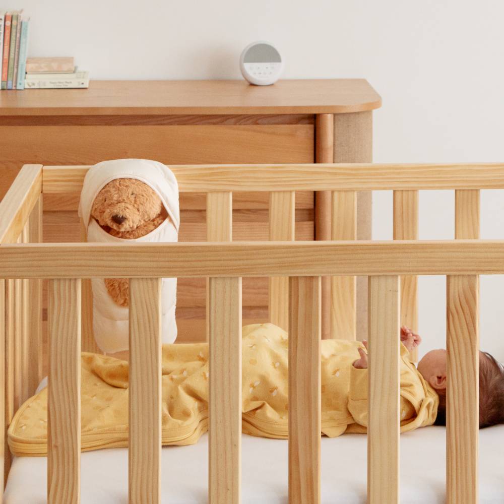 Wooden crib with a baby lying inside, white wall in the background