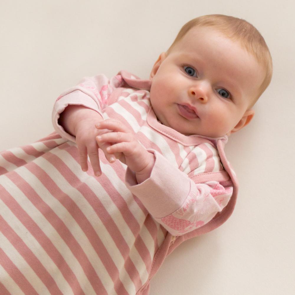 Baby wearing a pink and white striped woolbabe sleep sack on a plain background