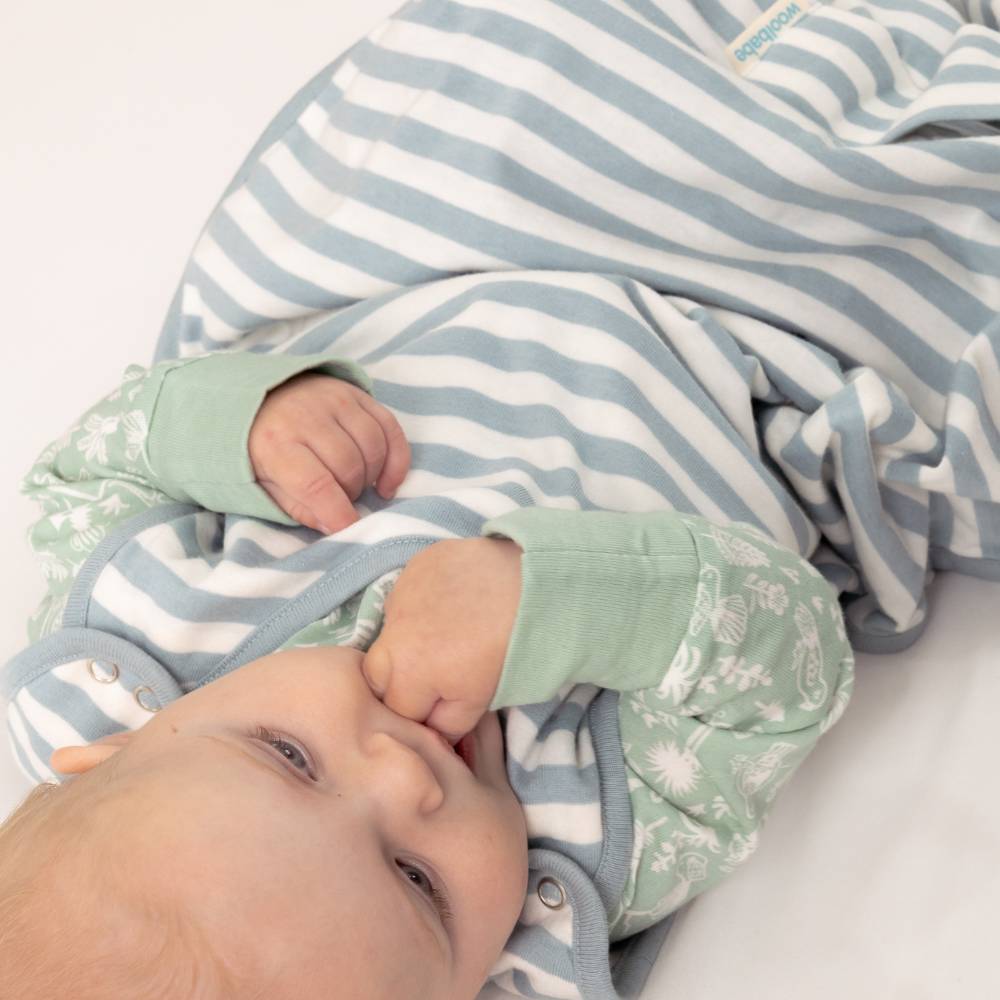 Baby wrapped in a blue and white striped blanket with green sleeves and pants.