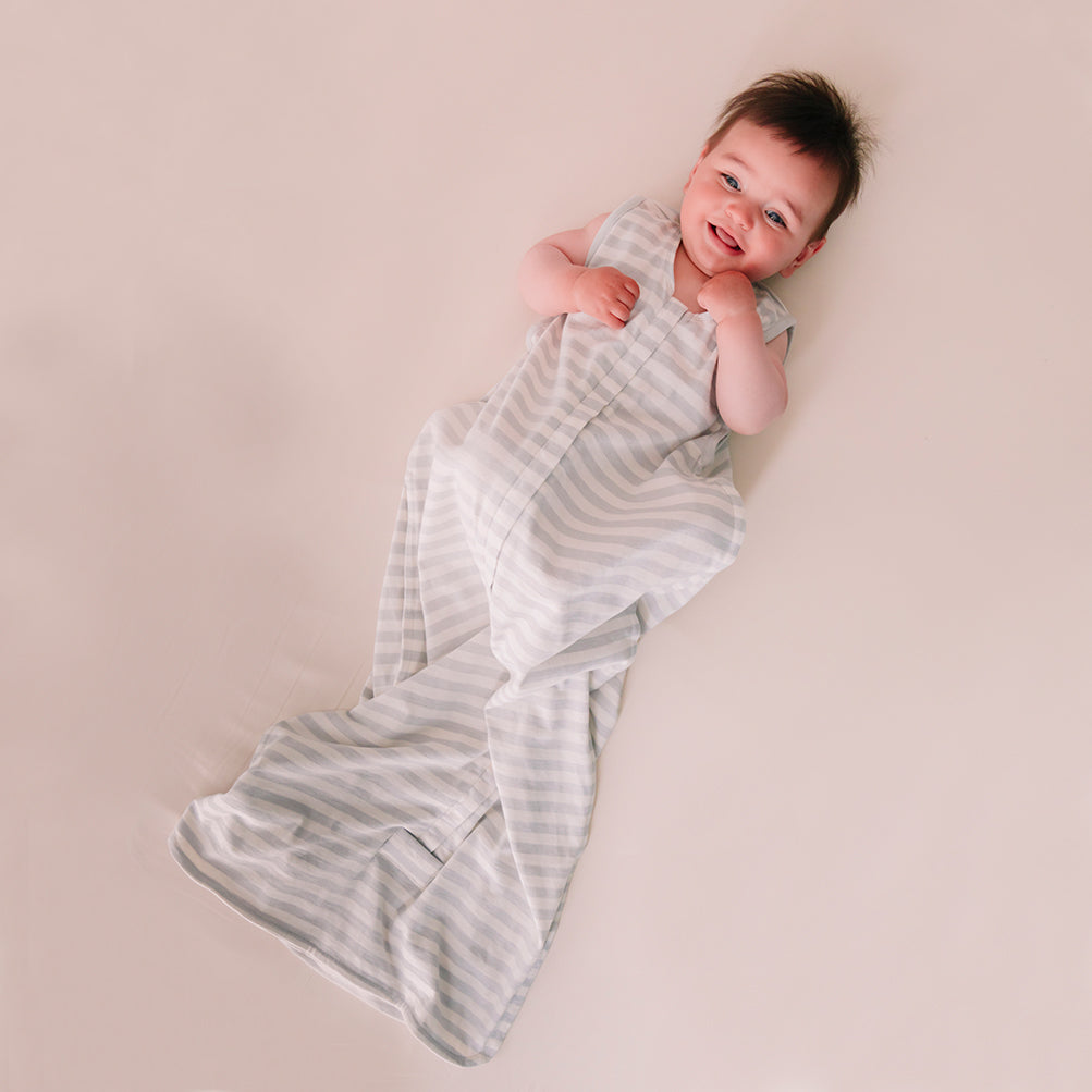 Newborn baby wrapped in a striped swaddle on a plain background