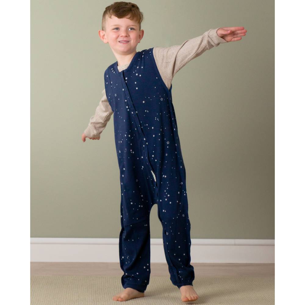 8 year old child wearing a navy blue onesie with star patterns against a plain wall.
