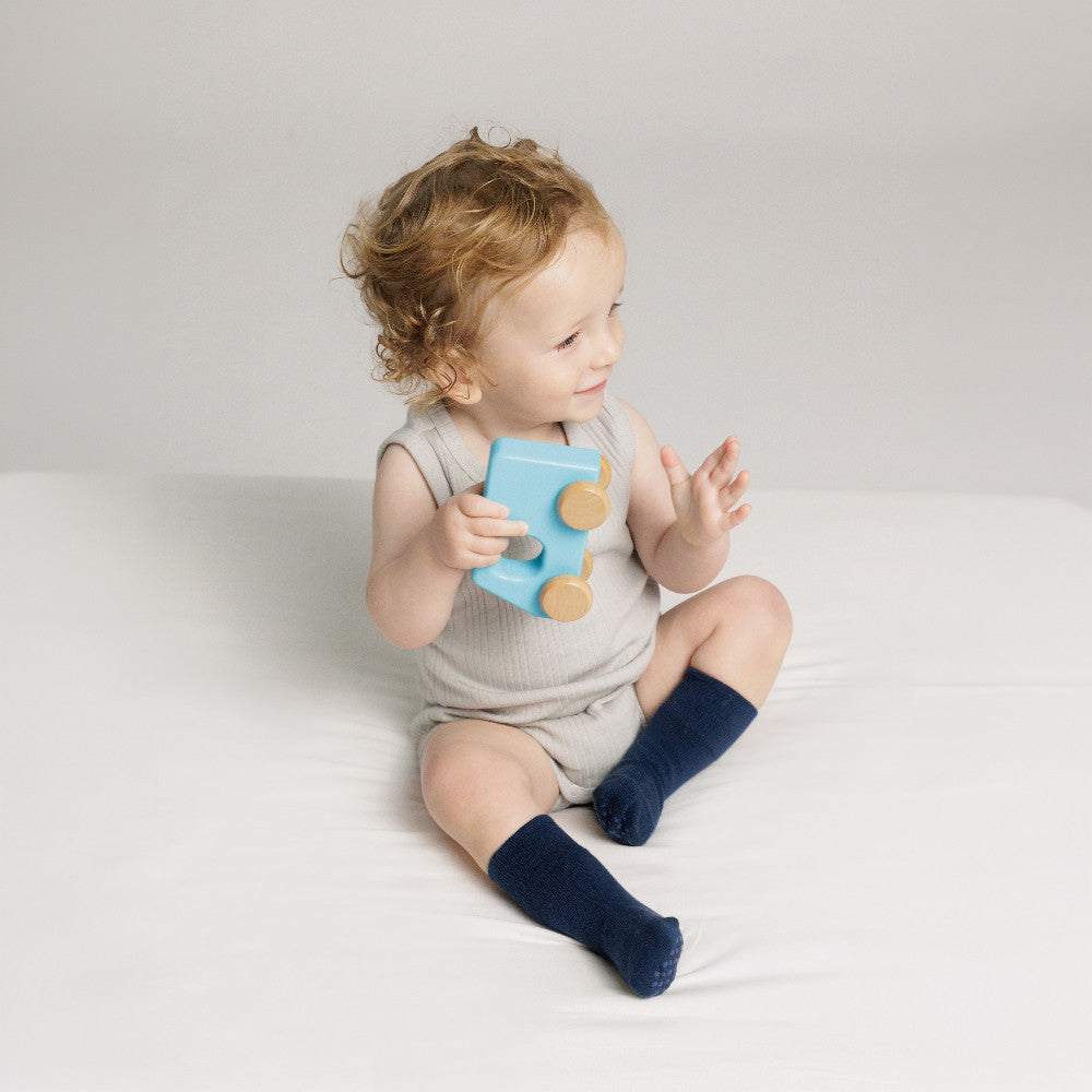 Baby wearing a pebble marl singletsuit and midnight navy blue Woolbabe Merino Socks. 