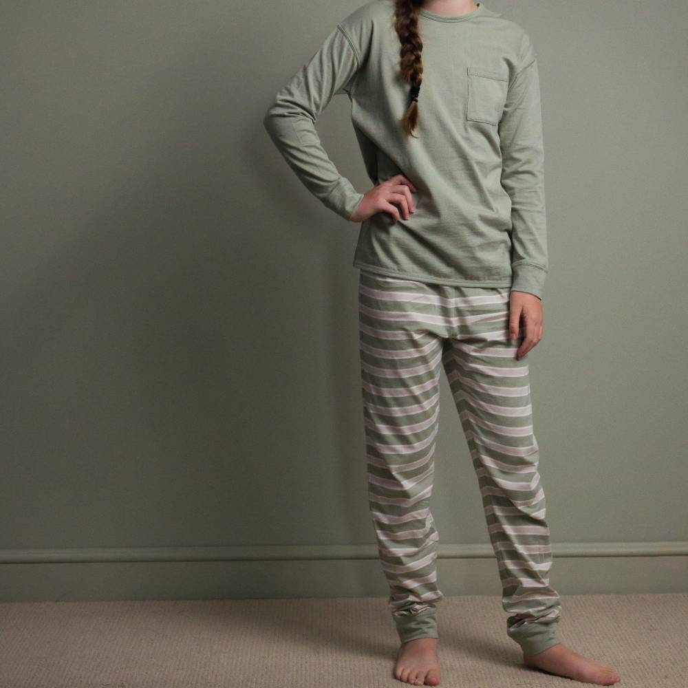 Person wearing a green long-sleeve top and striped pants against a plain background