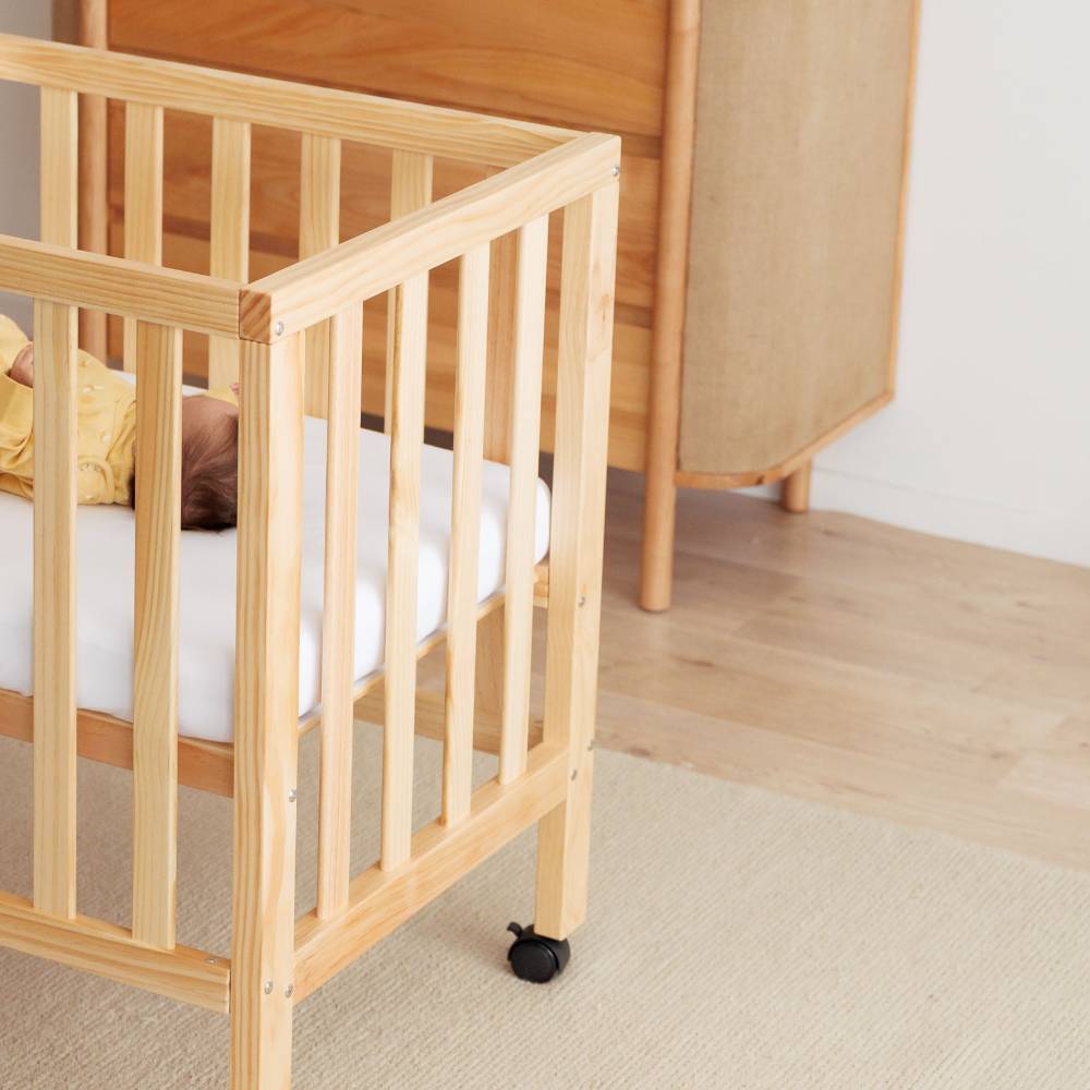 baby in small apartment sized wood cot on carpet and next to wood dresser