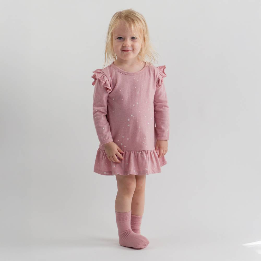 Young girl wearing a pink nightdress with ruffled sleeves and hem on a white background