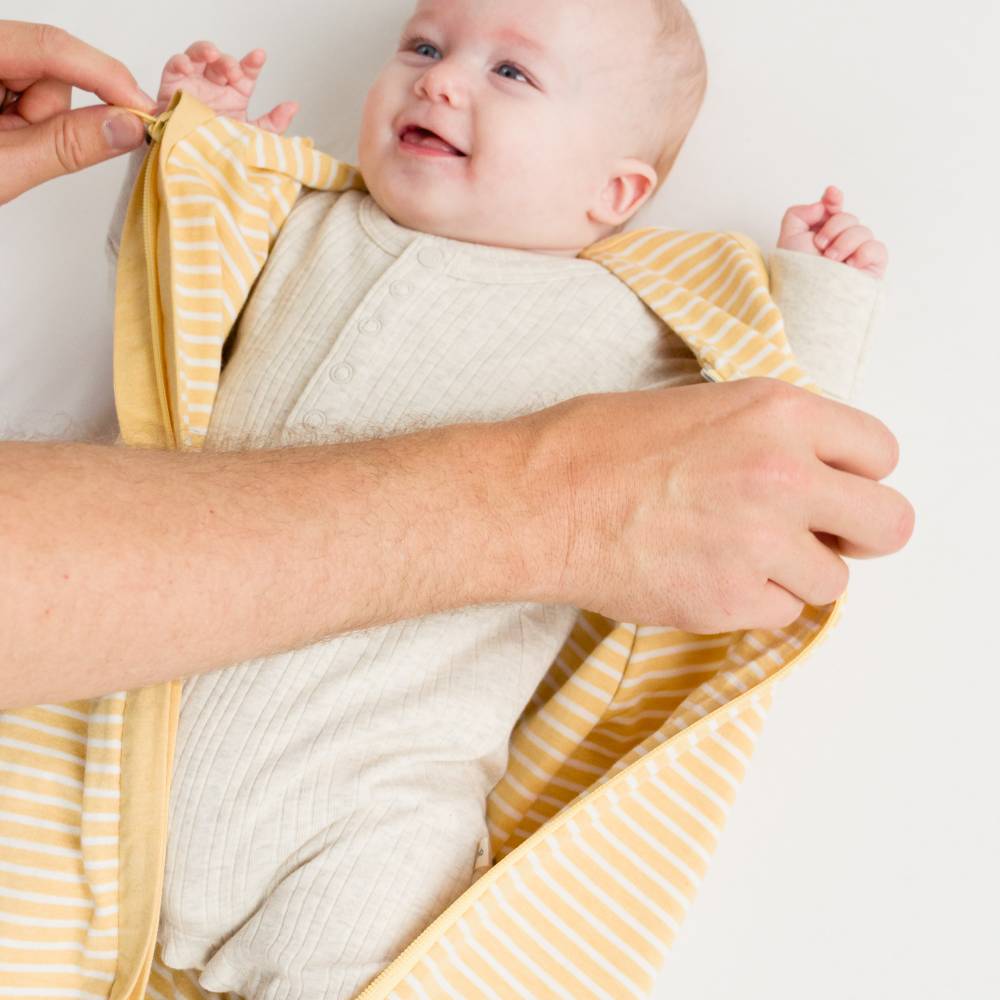 Baby wrapped in a yellow and white striped sleep sack with a person holding it