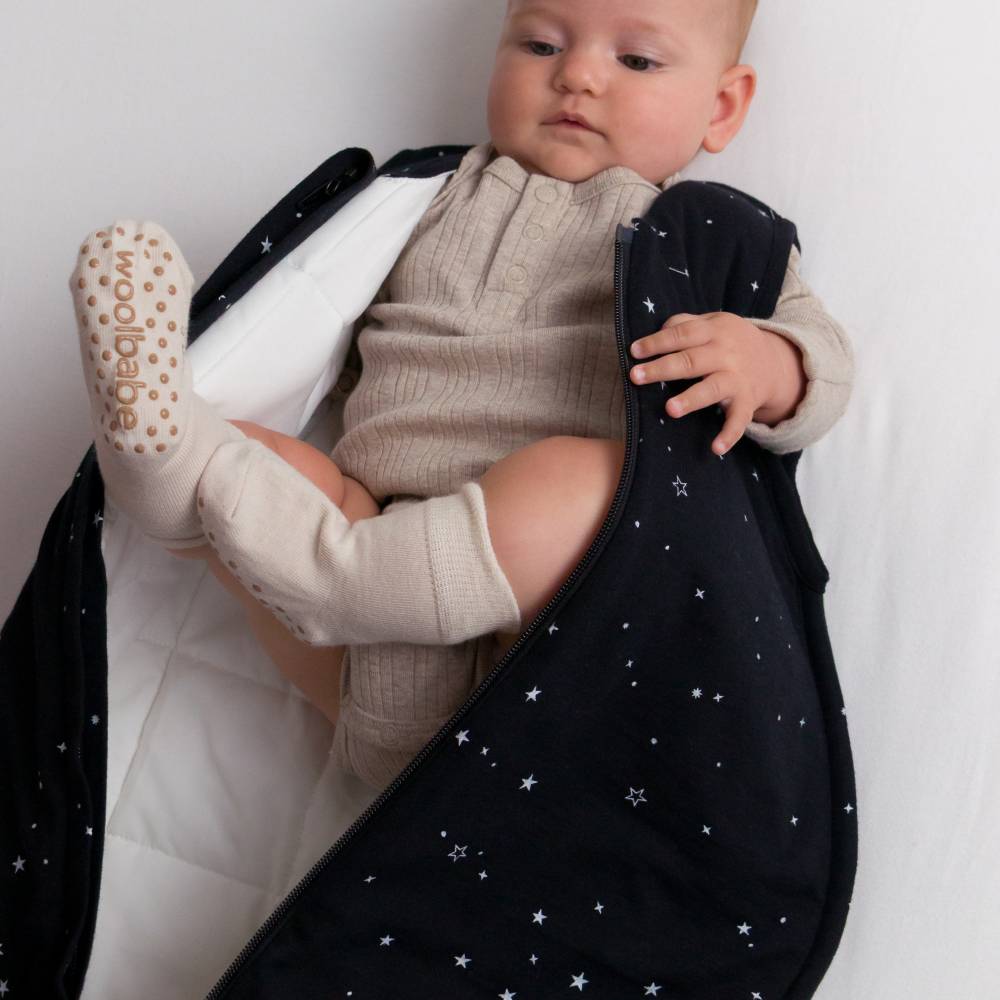 Baby wrapped in a black swaddle with star patterns, wearing woolbabe socks with brown grippy dots on the sole