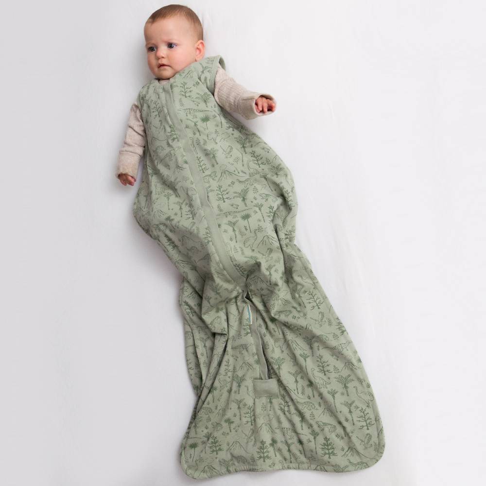 Baby wrapped in a green dino patterned sleep sack on a white background