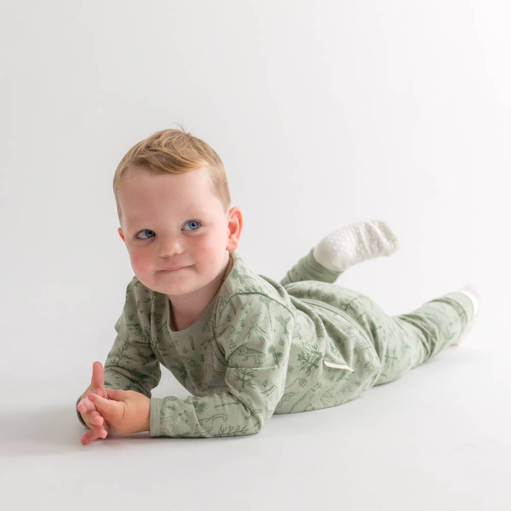 Baby in a green dinosaur pyjamas lying on a white surface