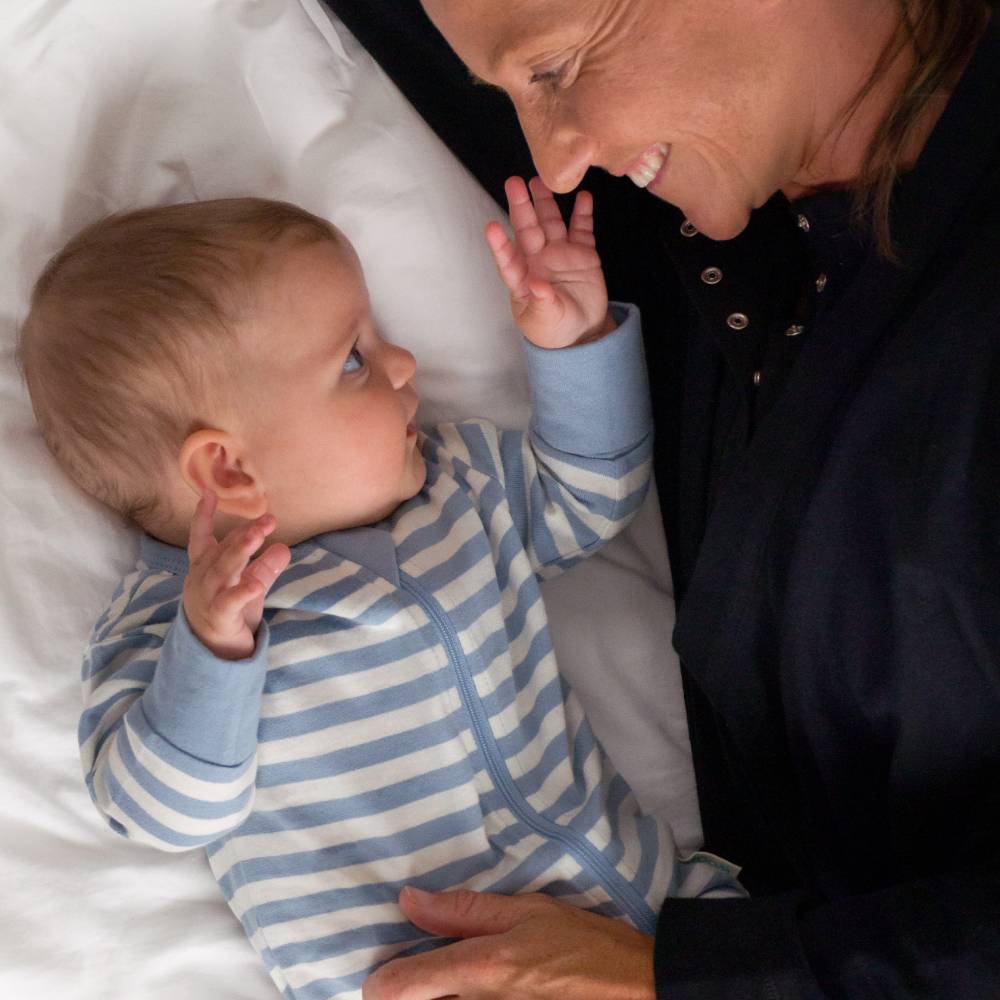 Baby in blue and white striped pajamas interacting with an adult on a white surface.