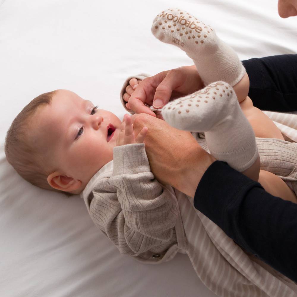 Baby lying on a white surface with a person helping to put on socks.