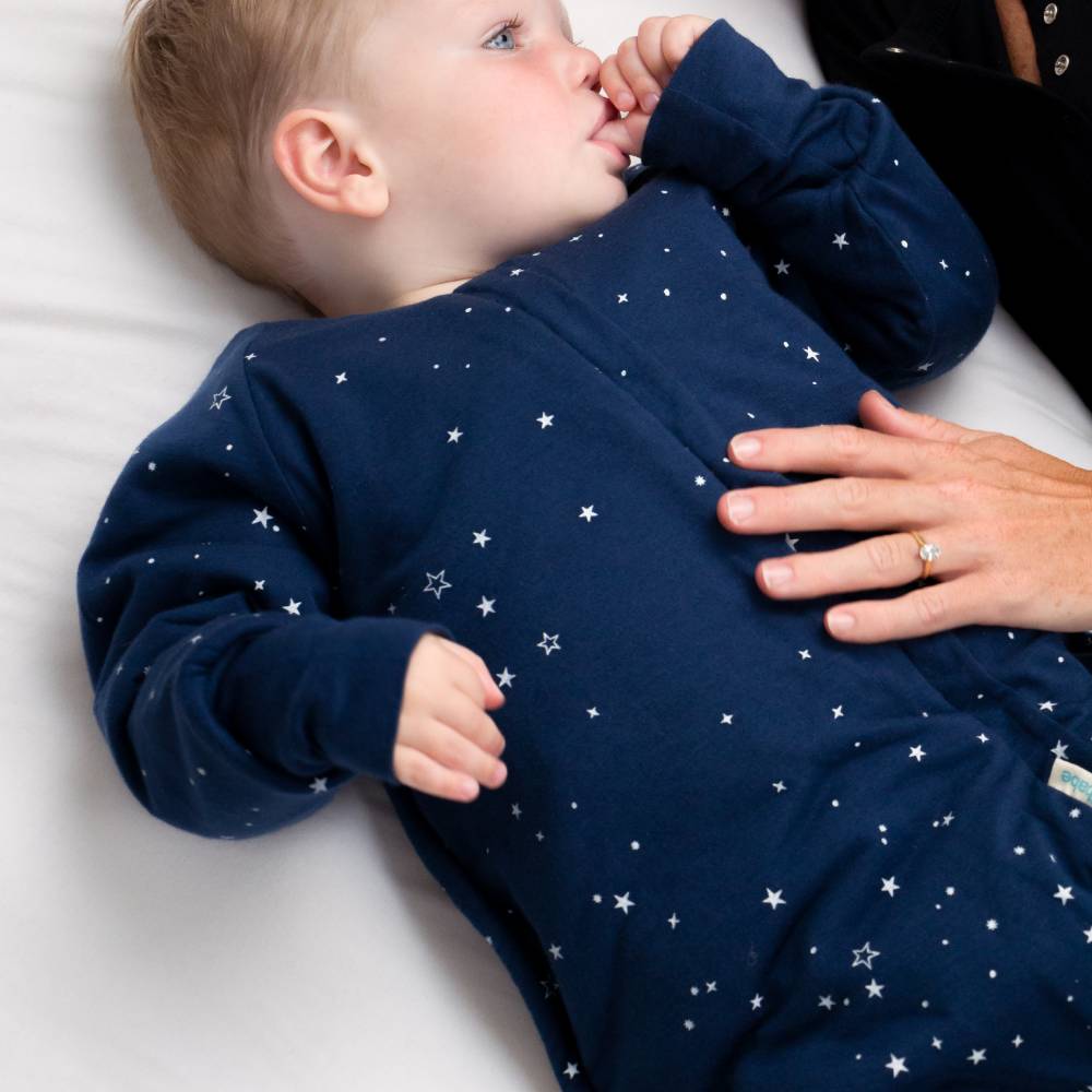 Baby wearing a navy blue onesie with star patterns, lying on a white surface.